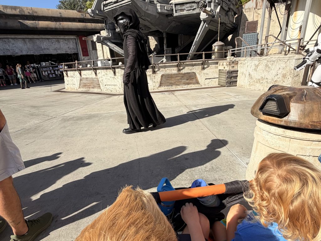 Two children sitting in front of a person dressed as Star Wars villain, Kylo Ren.