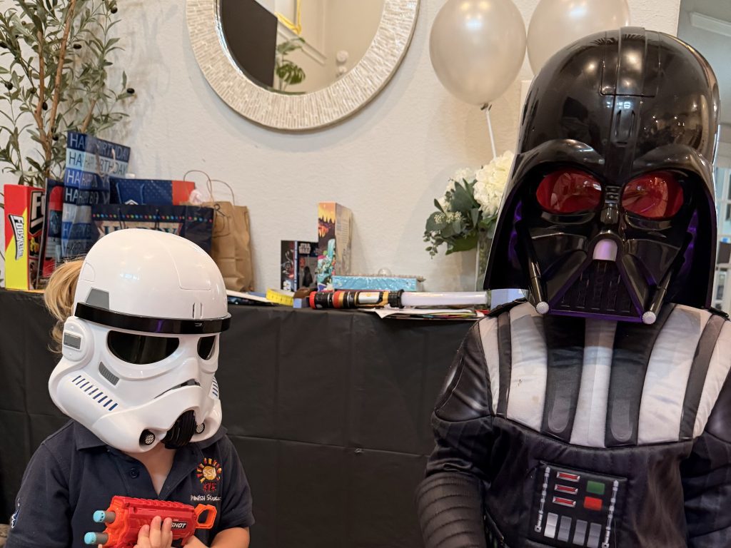 Two children wearing Star Wars costumes standing in front of a table with toys and party decorations.