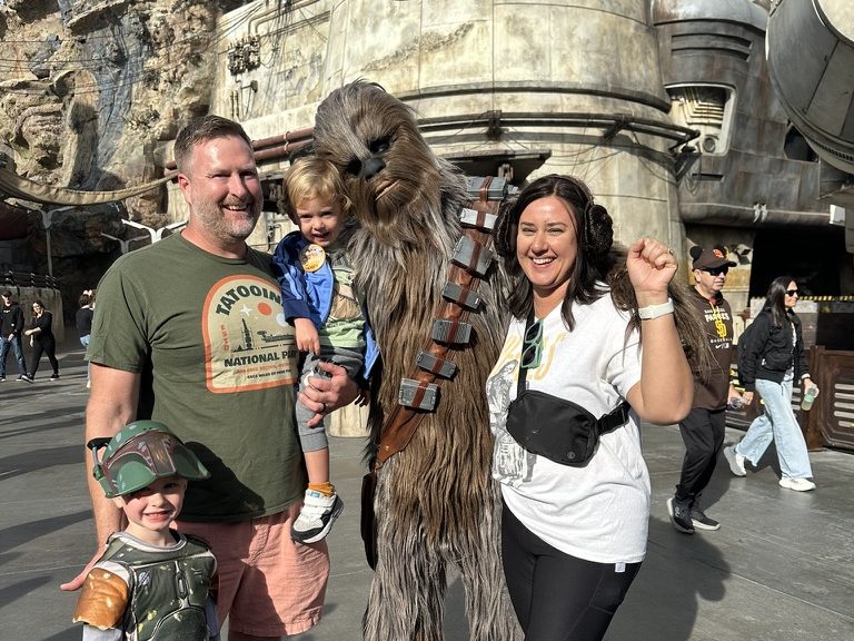 Family posing with Chewbacca in front of a Star Wars-themed building.