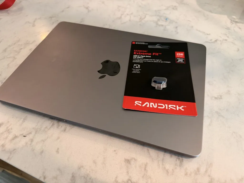 MacBook Air Storage Full - Here's How I Fixed It 3 Silver laptop with black and red SanDisk Extreme Fit USB-C drive packaging on a marble surface.