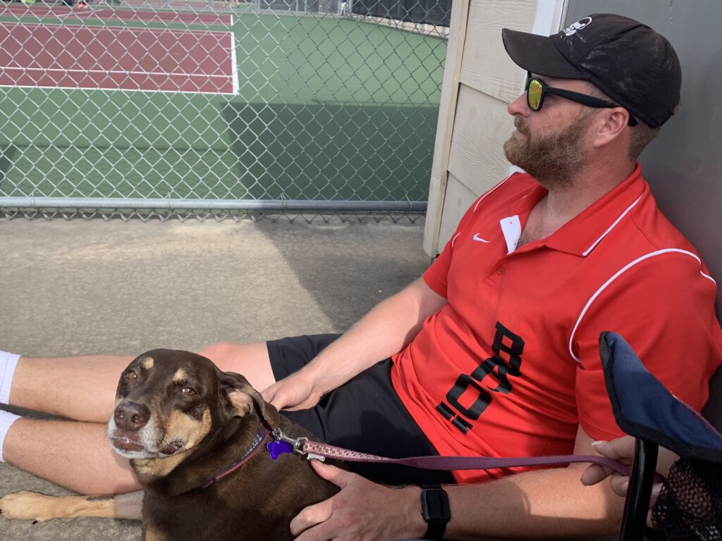 The Ghost of Past, Present, and Future at JS Wordsmith 3 A Man sitting with a dog by a tennis court