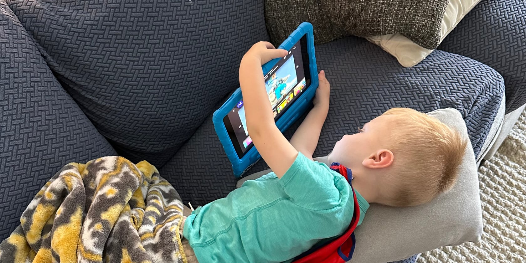 A toddler laying on a couch using a tablet