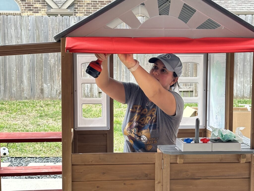 Threeanger Attitude and Spring Break Adventures 5 A woman using a drill inside a small play house.