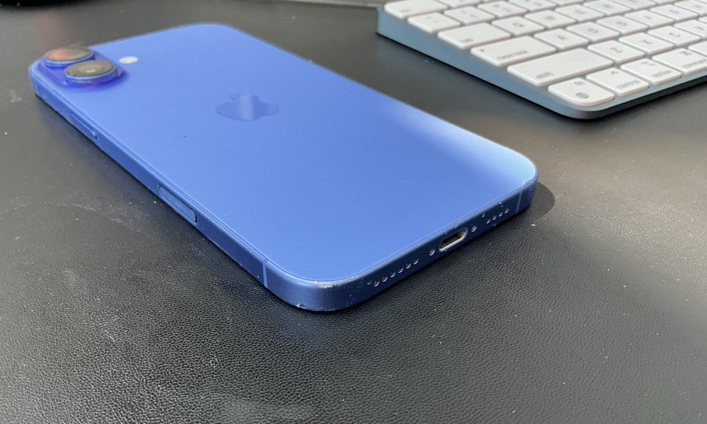 iPhone 16 Plus Review: A Year in Use and No Regrets 3 A blue iPhone 16 Plus on desk with Apple keyboard. The frame of the iPhone is scratched