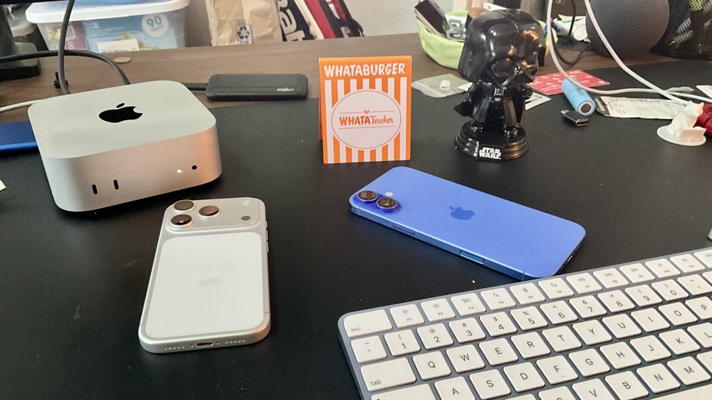First iPhone 17 Pro Impressions—A Writer’s Perspective 3 A silver iPhone 17 Pro on a desk with a blue iPhone 16 Plus, and Apple keyboard, and a Mac mini. Also on the desk are a Darth Vader bobble head figure and a whataburger number card.