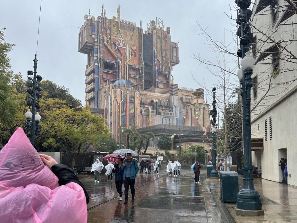 People walking in rain past a multi-colored building with spires.