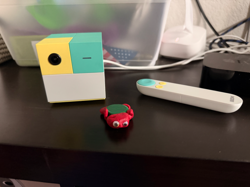 The NEX Playground, a colorful cube camera, red toy, and white remote on a dark surface.