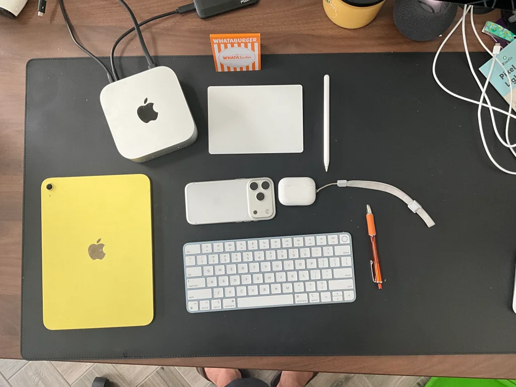 Black desk with Apple Mac Mini, keyboard, iPad, AirPods, and other tech items.
