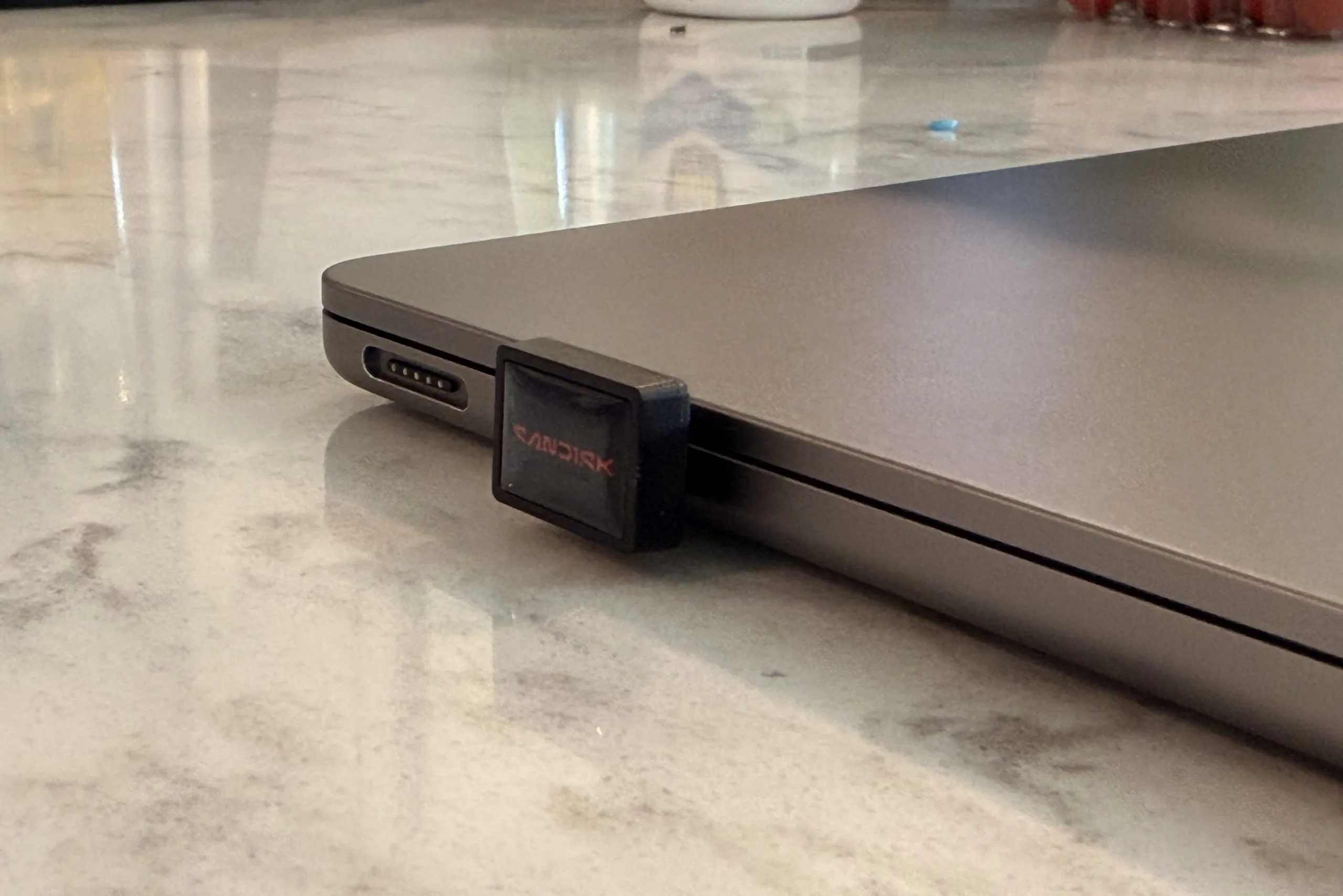 Macbook with extreme fit installed Sandisk USB drive plugged into a laptop on a marble countertop.