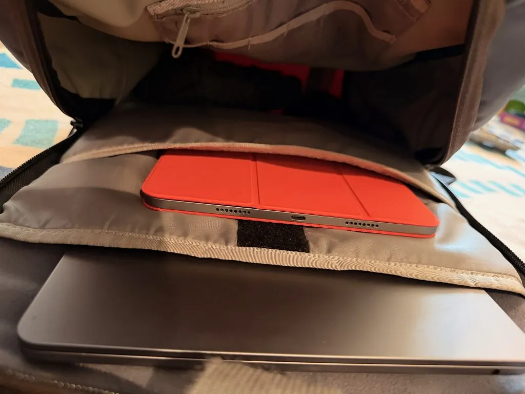 A view inside a writer's travel bag, showing a red iPad tucked into a sleeve and a gray MacBook placed below it.