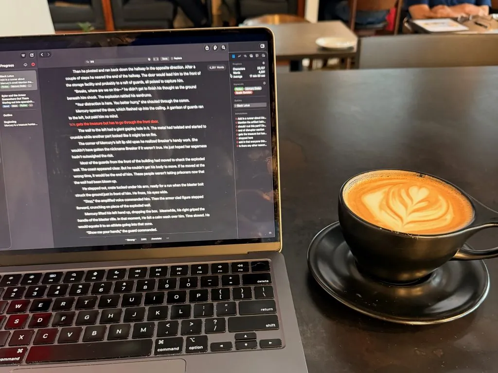 A MacBook Air displaying a text document, sitting on a dark surface next to a cup of coffee with latte art, as part of a MacBook buyer's guide for writers.